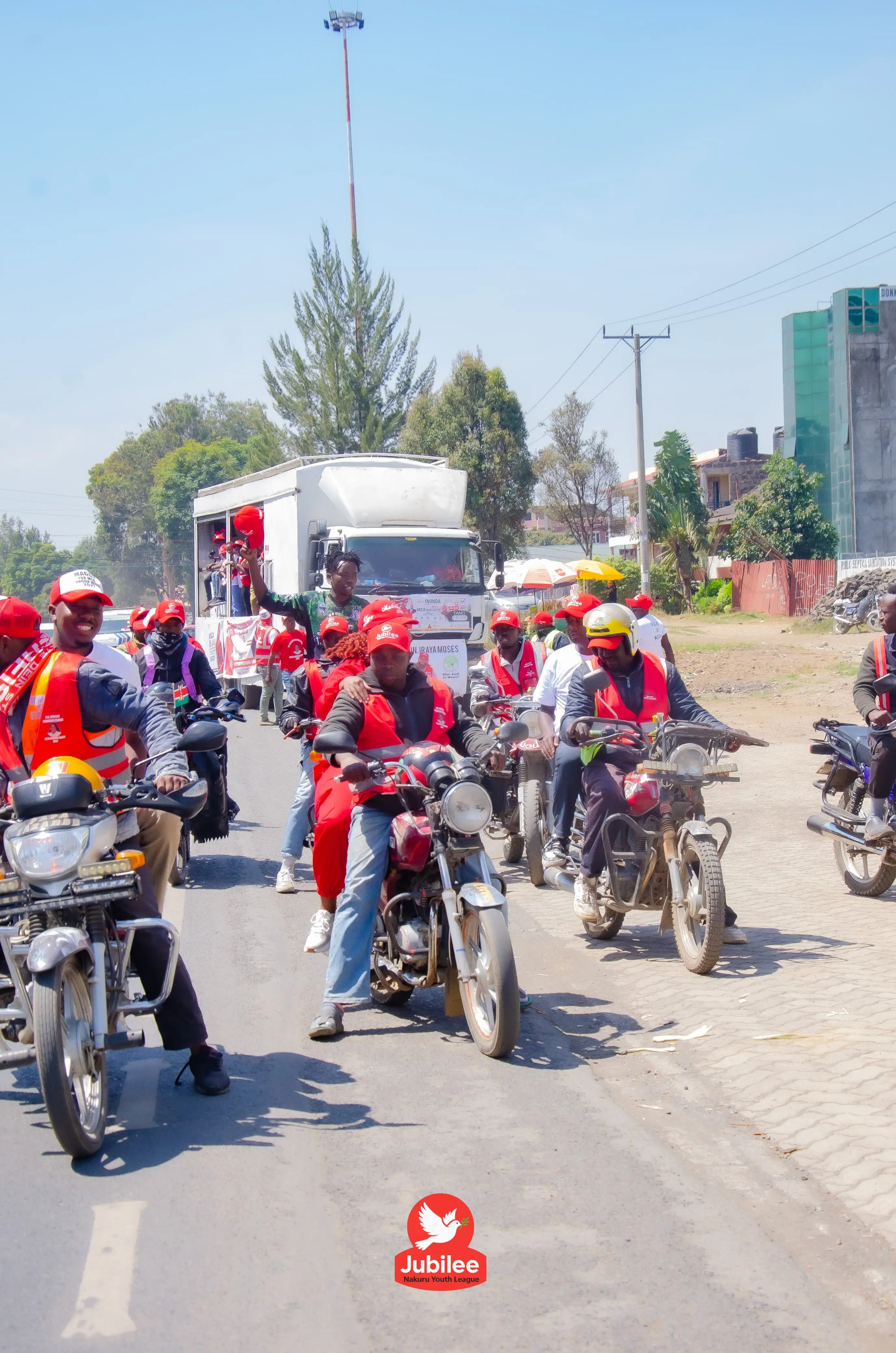 Line of boda boda riders in red caps riding down a road