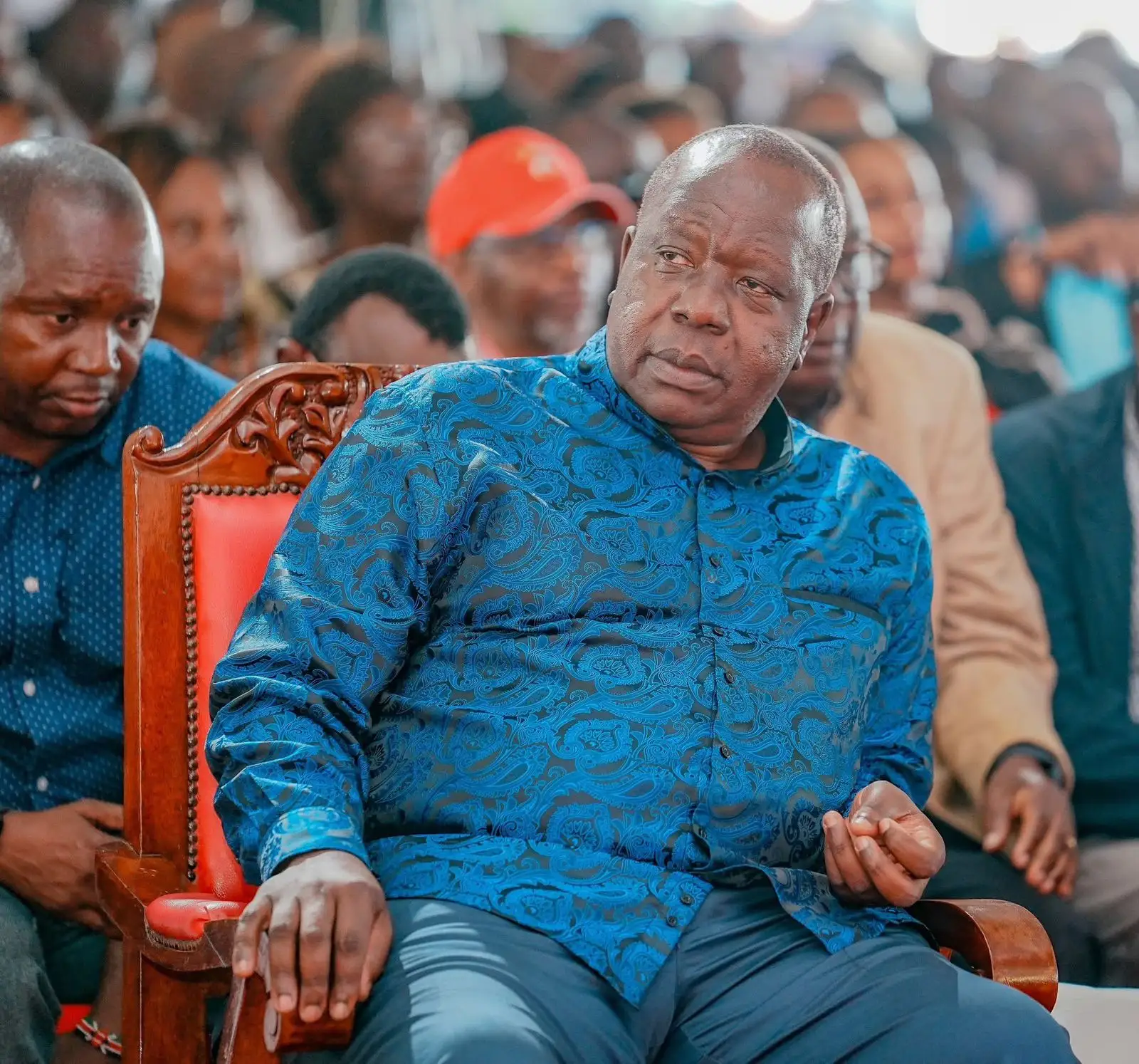 Dr Fred Matiang'i seated in a blue shirt at a public gathering