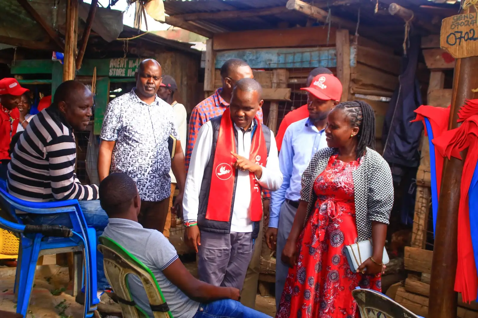 Team members in red sashes talking with traders at a market stall